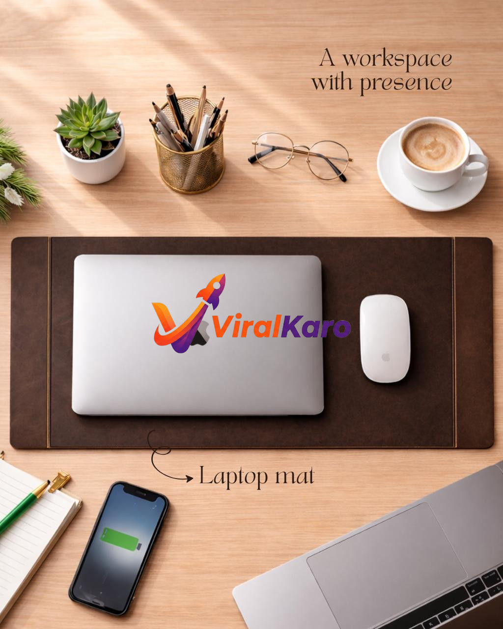Top-down view of a light wooden desk featuring a dark brown leather laptop mat with a silver MacBook Air, white Apple Magic Mouse, and a partially visible open MacBook Pro. To the left, a succulent plant in a white pot, a gold pen holder with pencils, a notebook with a green pen, and an iPhone with a charging battery icon are visible. To the right, round gold-rimmed glasses and a white cup of cappuccino complete the modern, organized workspace.